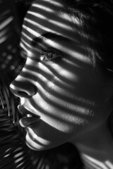 Obraz premium black and white portrait of female with shadow of a palm leaf on her face.