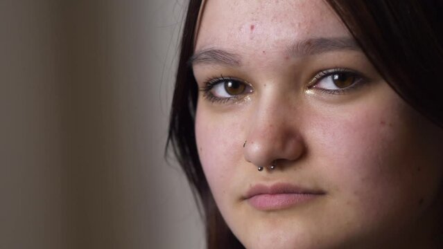 Studio shot Portrait of young gen z teen girl with dark hair and nose piercing looking at camera. Head shot close up portrait. 4K slow motion video