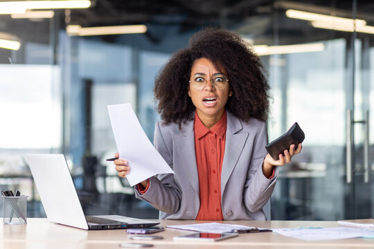 A frazzled businesswoman looks overwhelmed as she juggles paperwork and a phone call at her office desk. The image conveys a sense of stress, multitasking, and the busy nature of corporate life.