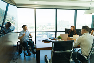 Disabled man in a wheelchair speaking to a group of people in a meeting room