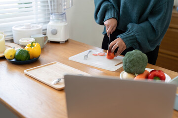 Woman chopping vegetables by laptop on hardwood countertop