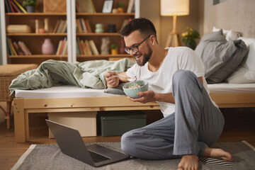 Young man with laptop having breakfast in bedroom