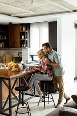 Cheerful couple enjoys a light-hearted moment in their sunny kitchen, working on laptop surrounded by a healthy breakfast