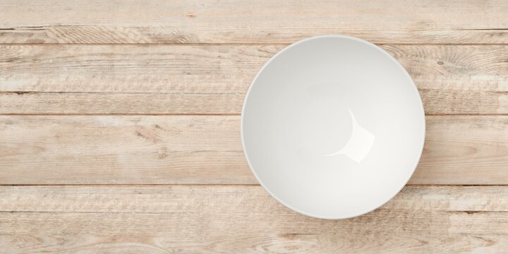 Single empty white porcelain bowl or dish on wooden table background with copy space, flat lay top view from above