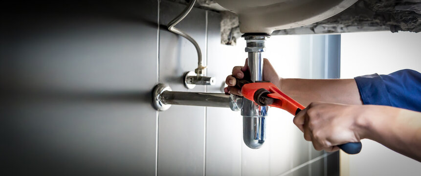 Plumber uses wrench to repair water pipe under sink There is maintenance to fix the water leak in the bathroom.with red wrench, plumbing install concept.