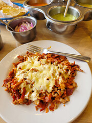 Plate of Spicy Al Pastor topped with cheese, served with fresh salsa and onions, vertical