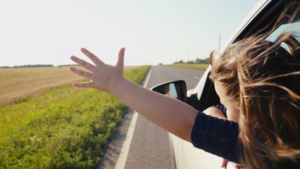 Young girl schoolgirl daughter driving car with hand out window, child hair fluttering iwind, kid child enjoying sun travel travel, vacation time, feeling freedom joy, looking road ahead, childhood