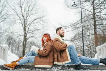 Obraz premium Love romantic couple lovestory. Brutal bearded man, bright red-haired girl woman in winter park. Romantic date, kissing, hugging. Walking, having fun. Stylish clothes, red sheepskin coat, jacket, hat
