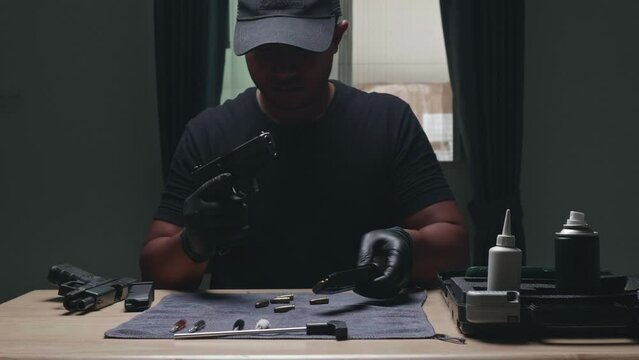 Slow motion image of a man sitting alone in a room. He would disassemble and clean a 9 mm semi-automatic pistol. assembling the gun. military ammunition. weapon care.