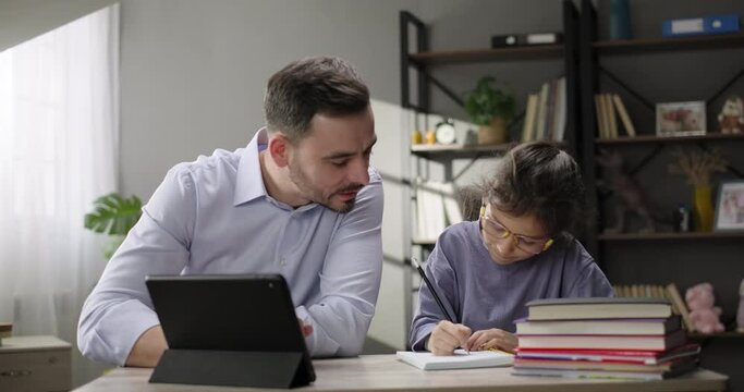 Happy family. Father helping daughter doing homework at home desk, studying online with digital tablet. Private tutor teaches preteen girl individually. Private education