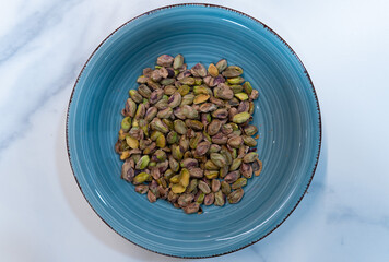 A blue bowl filled with pistachios. The bowl is on a white surface