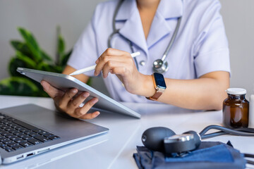 Cropped image of female doctor taking note on digital tablet, working on laptop computer recording patient information in medical office in hospital.