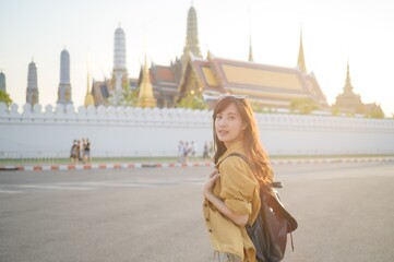 Traveler asian woman in her 30s, backpack slung over her shoulder, explores the intricate details of Wat Pra Kaew with childlike wonder. Sunlight dances on the golden rooftops.