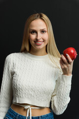 Beautiful young woman with a red apple on a black background. - 750020677