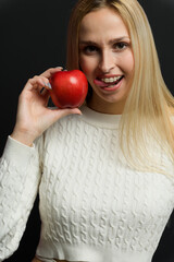 Beautiful young woman holds an apple near her face, smiles, looks at the camera. - 750020679
