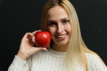 Beautiful young woman holds an apple near her face, smiles, looks at the camera. - 750020681
