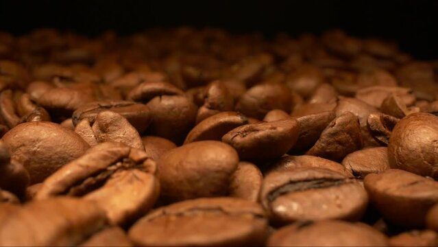 Freshly roasted coffee beans macro closeup shot on dark background tracking shot