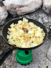Frying potatoes on a tourist gas stove in a frying pan in nature