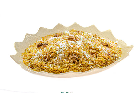 Rfiss, Algerian traditional semolina-based dessert, enriched with dried fruit and whole nuts, sprinkled with powdered sugar. Served on a decorative plate, side view isolated on a white background