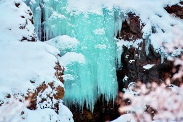 Frozen waterfall with icicles surrounded by snow-covered rocks Location: Hraunfossar, Iceland.