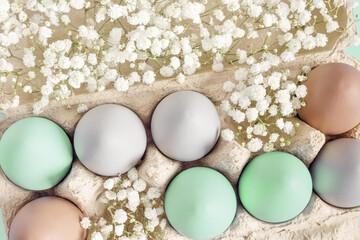 Pastel Easter Eggs with white Flowers in Carton box on mint Background, top view chicken egg painted turquoise beige colors. Easter celebration concept. Festive food, minimal still life holiday