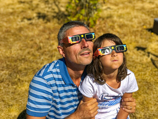 Father and daughter, family viewing solar eclipse with special glasses in a park - obrazy, fototapety, plakaty
