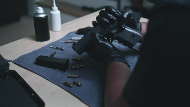 Slow motion image of a man sitting alone in a room. He would disassemble and clean a 9 mm semi-automatic pistol. assembling the gun. military ammunition. weapon care.