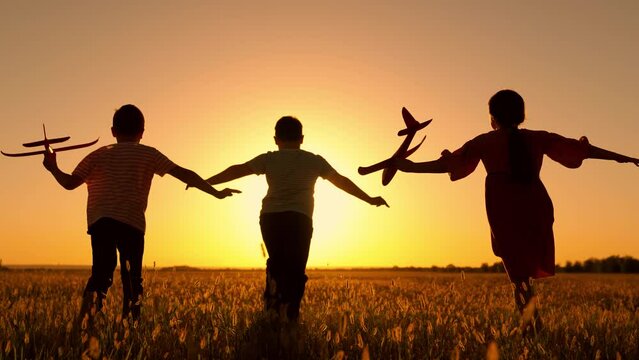 Happy children run with toy plane across field at sunset. Boy, girl wants to become pilot, an astronaut. Children play with toy plane. Slow motion. Teenager dreams of flying, becoming pilot. Children