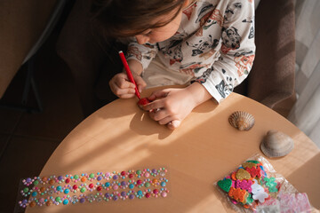 Child girl doing creative crafts at home on sea shells, colouring and making stickers. 