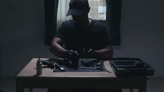 Slow motion image of a man sitting alone in a room. He would disassemble and clean a 9 mm semi-automatic pistol. assembling the gun. military ammunition. weapon care.