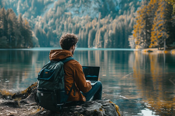 a young creative sitting by a lake and working on laptop