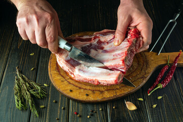 The chef uses a knife to cut the meat from the bone on a kitchen board before preparing the dish....