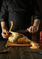 The chef tries to cut off a leg of raw chicken with a knife on the kitchen table. Concept of...