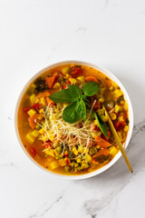 Minestrone soup from zucchini and tomato, onion and carrot, corn and peas with parsley, top view of bowl of soup garnished with parmesan and basil, vegetarian soup