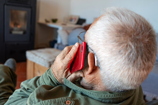 Detail of unrecognisable old man with his back turned talking on the telephone, hearing aid in his ear. Dressed in green shirt, grey hair