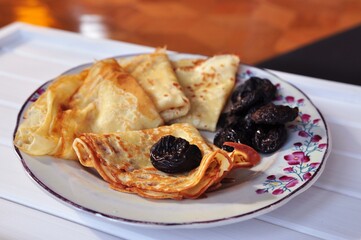 Delicious pancakes dessert for breakfast. Sweet pancakes with prunes on the plate with flowers on white table. Tasty food of Ukrainian cuisine. 