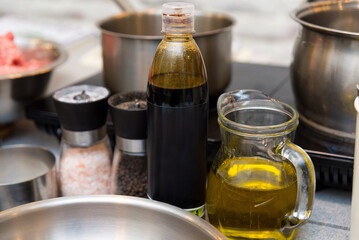 Cooking Oil and Seasonings in Kitchen Setting. A culinary setup with olive oil in a clear glass jug, vinegar in a bottle, and salt and pepper grinders, ready for food seasoning.