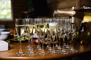 Pouring Champagne into Glasses for Celebration. Champagne being poured into elegant flutes, set on a wooden table, ready for a festive toast or celebration.
