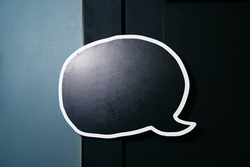Blank Speech Bubble on Dark Background. Empty speech bubble sign hanging on a dark paneled wall,...