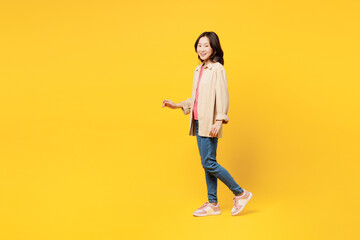 Fototapeta na wymiar Full body side profile view young woman of Asian ethnicity she wearing pink t-shirt beige shirt pastel casual clothes walk go isolated on plain yellow background studio portrait. Lifestyle portrait.
