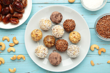 Healthy raw energy balls. Candy vegan balls of dates, nuts and coconut on plate on blue background. Top view, concept of useful home-made candies without sugar