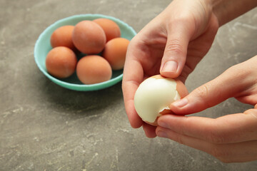 Woman peeling boiled egg on grey background, closeup