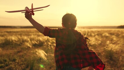 Happy kid runs with toy airplane on field in sunset light. Child play toy airplane. Little girl...