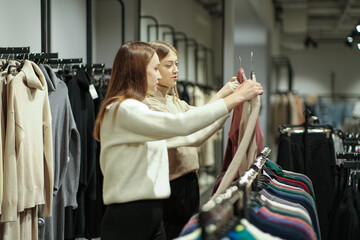 Portrait of smiling two young women shopping together in a boutique and choosing clothes. Two women...