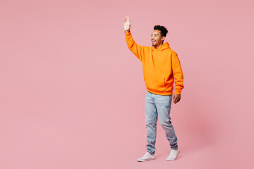 Full body side profile view young man of African American ethnicity he wears yellow hoody casual clothes walk go waving hand isolated on plain pastel light pink background studio. Lifestyle concept.