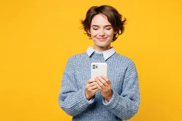 Foto op Plexiglas Young smiling happy woman she wearing grey knitted sweater shirt casual clothes hold in hand use mobile cell phone chat online isolated on plain yellow background studio portrait. Lifestyle concept. © ViDi Studio