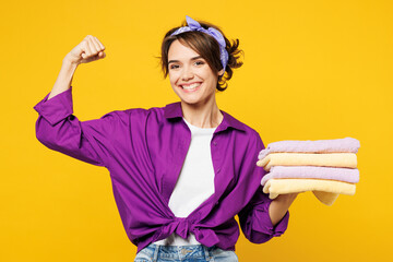Young string happy smiling woman wears purple shirt do housework tidy up hold pile of towels after...