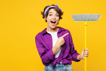 Young happy woman wears purple shirt casual clothes do housework tidy up hold in hand point index...