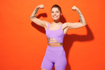 Young happy fitness trainer instructor sporty woman sportsman wear purple top clothes spend time in home gym show muscles look camera isolated on plain orange background Workout sport fit abs concept