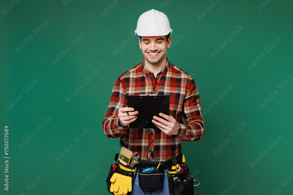 Poster Young employee laborer man wear red shirt hardhat hat work hold clipboard read paper documents isolated on plain green background. Instruments accessories for renovation apartment Repair home concept